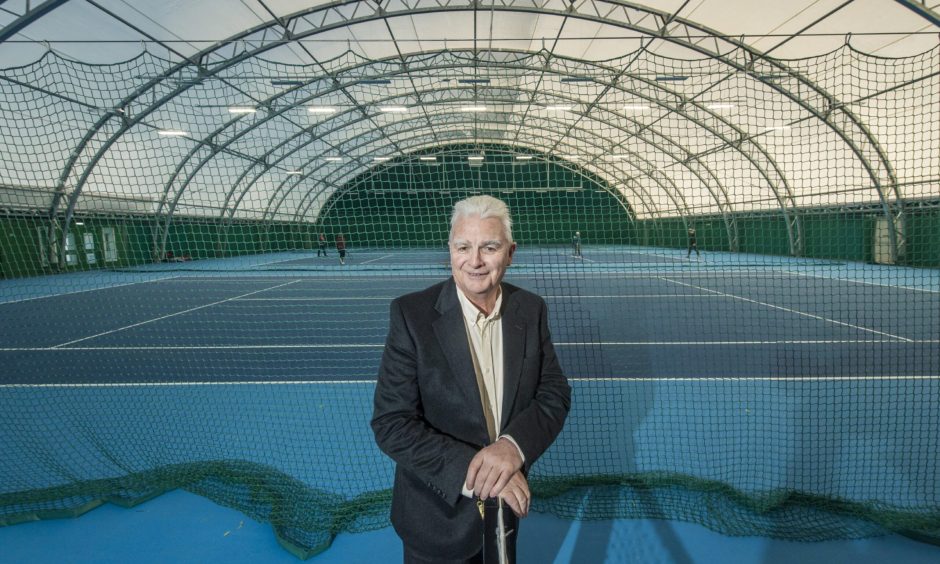 Sandy Adam at net of indoor tennis court. 