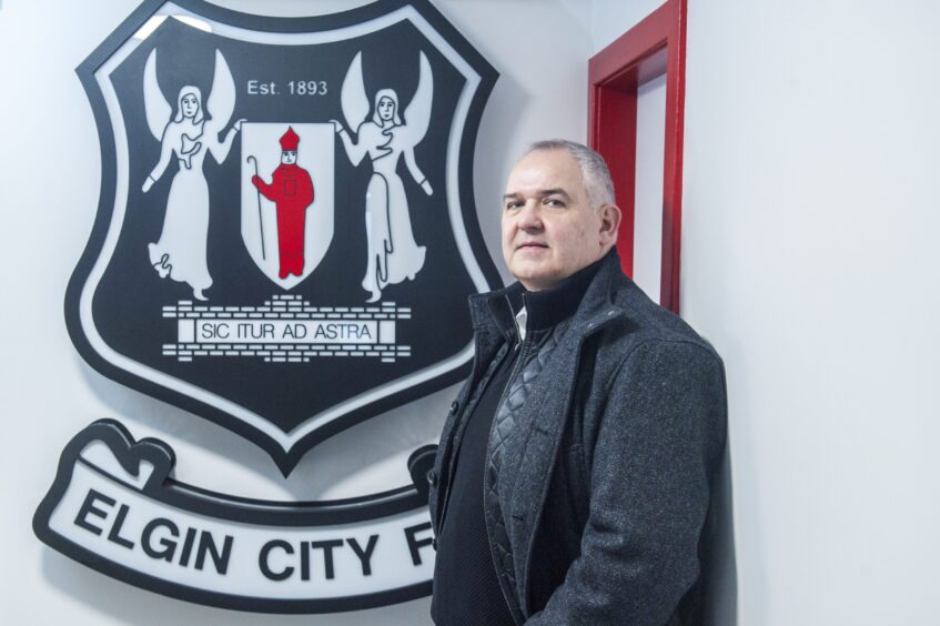 Chairman Alan Murray stands in front of the Elgin City badge.