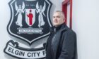 Chairman Alan Murray stands in front of the Elgin City badge.
