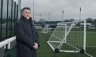 Dave Allen leaning on barrier next to football pitch.