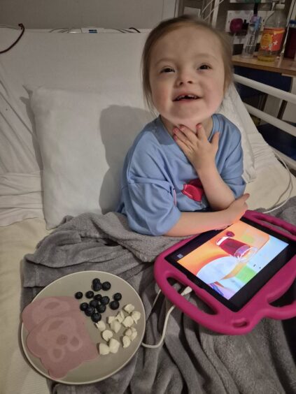 Jaylin with an eye pad in a pink cover sitting in a hospital bed.