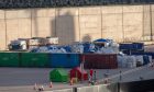 Charred cargo from the vessel's hold can be seen on the quayside, ringed by shipping containers of varying colours.