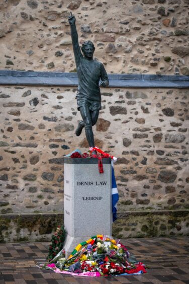 The Denis Law statue at Marischal Square, which depicts the star in iconic pose, bedecked in floral tributes.