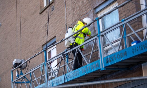 workers on a gantry power-clean an Aberdeen high-rise that will soon have giant murals of Denis Law painted on the side.