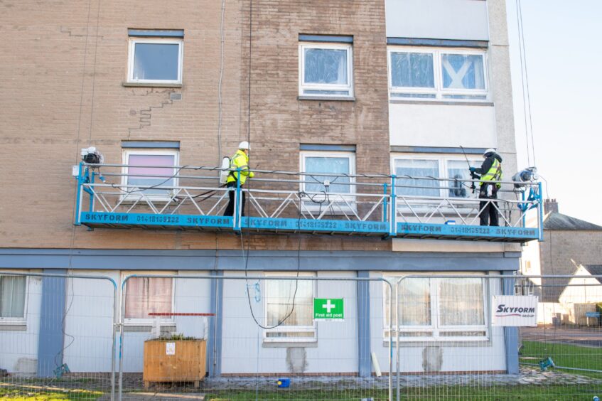 Workers in high-vis jackets spray clean the sides of Clifton Court from a gantry in preparation for the painting of giant murals paying tribute to Denis Law.