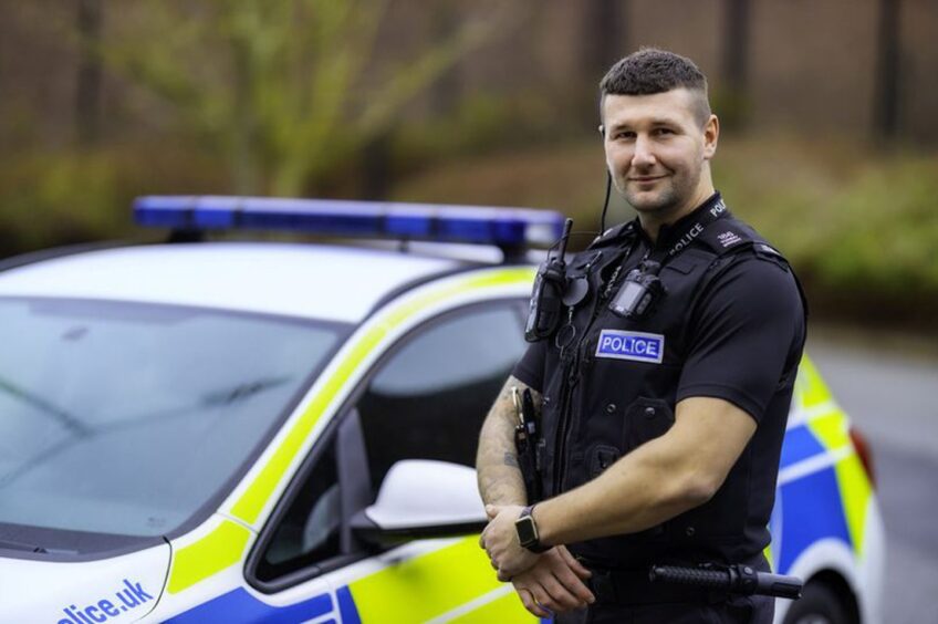 Former Dons striker Tommy Wright, who now works as an officer for Leicestershire Police, pictured in his uniform standing beside a police car