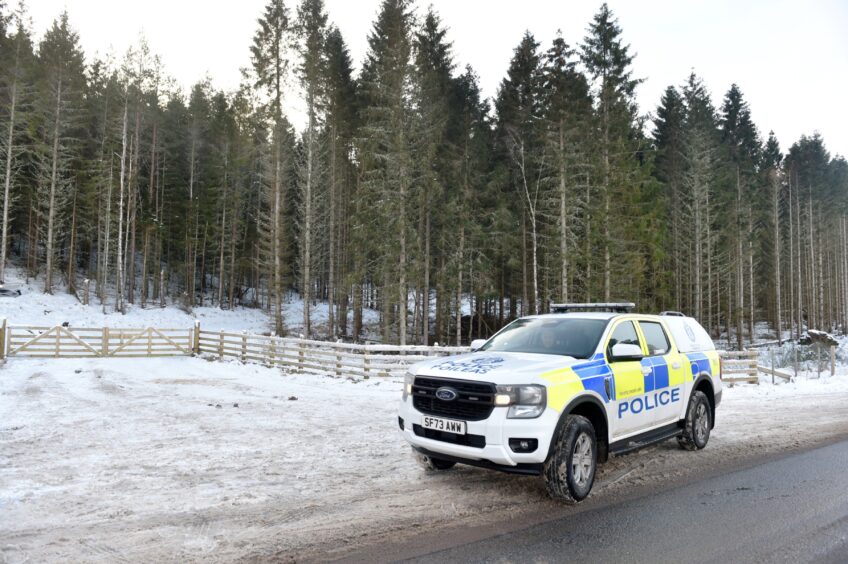 Police vehicle in the snow along a tree lined road.