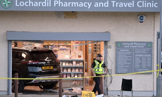 Police stand guard outside Lochardil Pharmacy where a black Nissan crashed through the front door.