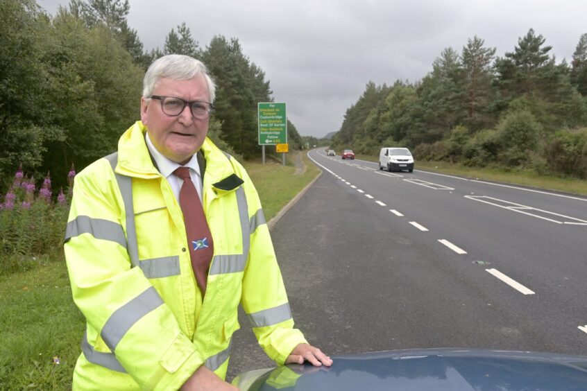 Fergus Ewing pictured in a yellow fluorescent coat, beside car in a layby on the A9 near Aviemore.