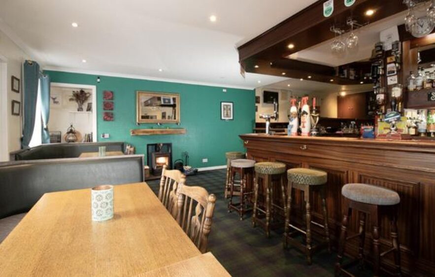 The bar to the right with bar stool as large dining table sits to the left. Th bright green wall to the rear of the image has a log burner. 