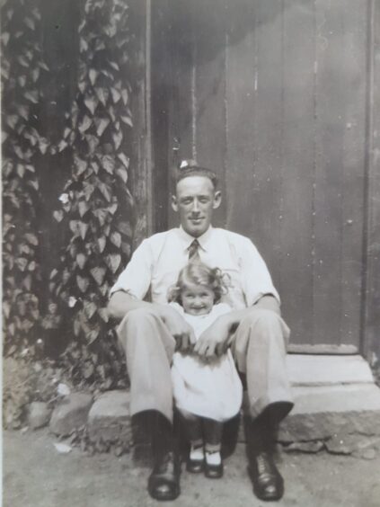 Sheila pictured with her father, sitting on the steps outside a wooden door.