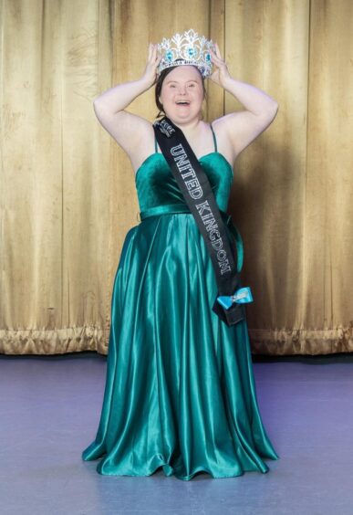 Taylor, dressed in a long green dress and a black sash, holding a silver crown on her head.