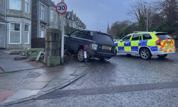 A black Range Rover and police car at the scene of the Great Western Road crash. The Range Rover has crashed through the garden wall and into the garden of a residential property there. The car is resting on top of some of the rubble.