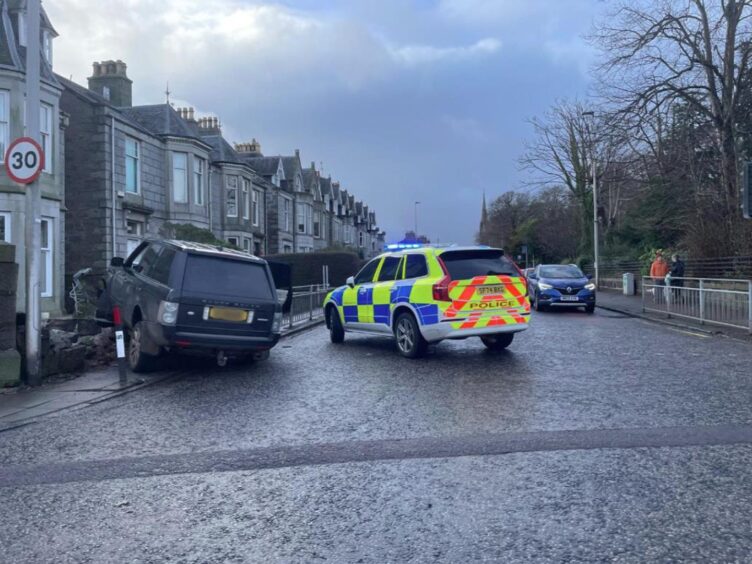 Pictures shows a crash on Great Western Road in Aberdeen, with a black Range Rover beached on top of a demolished garden wall, debris left in the garden. A police car is blocking the road.