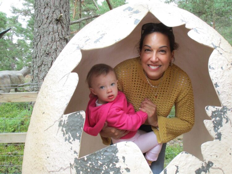 Christina in a yellow jumper holding her daughter in her arms. 