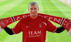 Tommy Wright wearing a Dons shirt and holding a scarf up at Pittodrie after he signed for Aberdeen FC