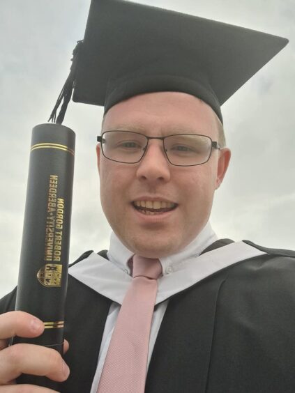 Conner Ladley wearing his graduation cap, gown while holding his scroll. 