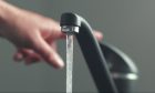 A hand turning off a running tap.