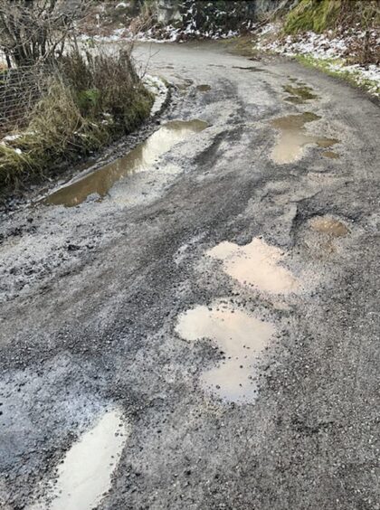 The road is covered in potholes, many filled with puddles of water.