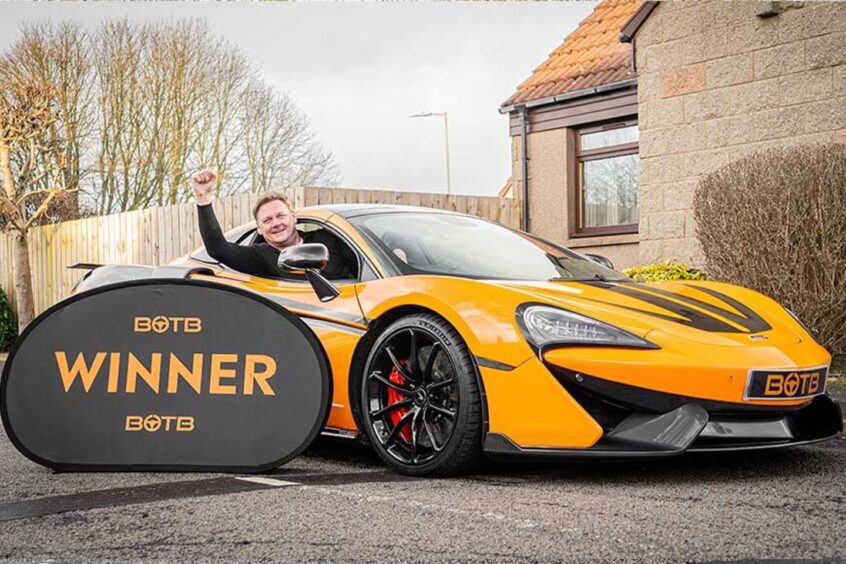 David sitting inside his new supercar and raising his arm in triumph out of the window