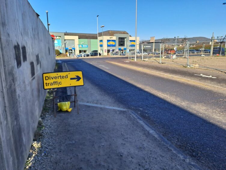 Yellow diverted traffic sign located on the bus lane with Rose Street Retail Park up ahead.