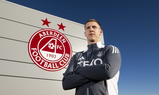 Aberdeen new signing Mats Knoester stands beside the club's badge which is displayed on a wall at the Cormack Park training complex.