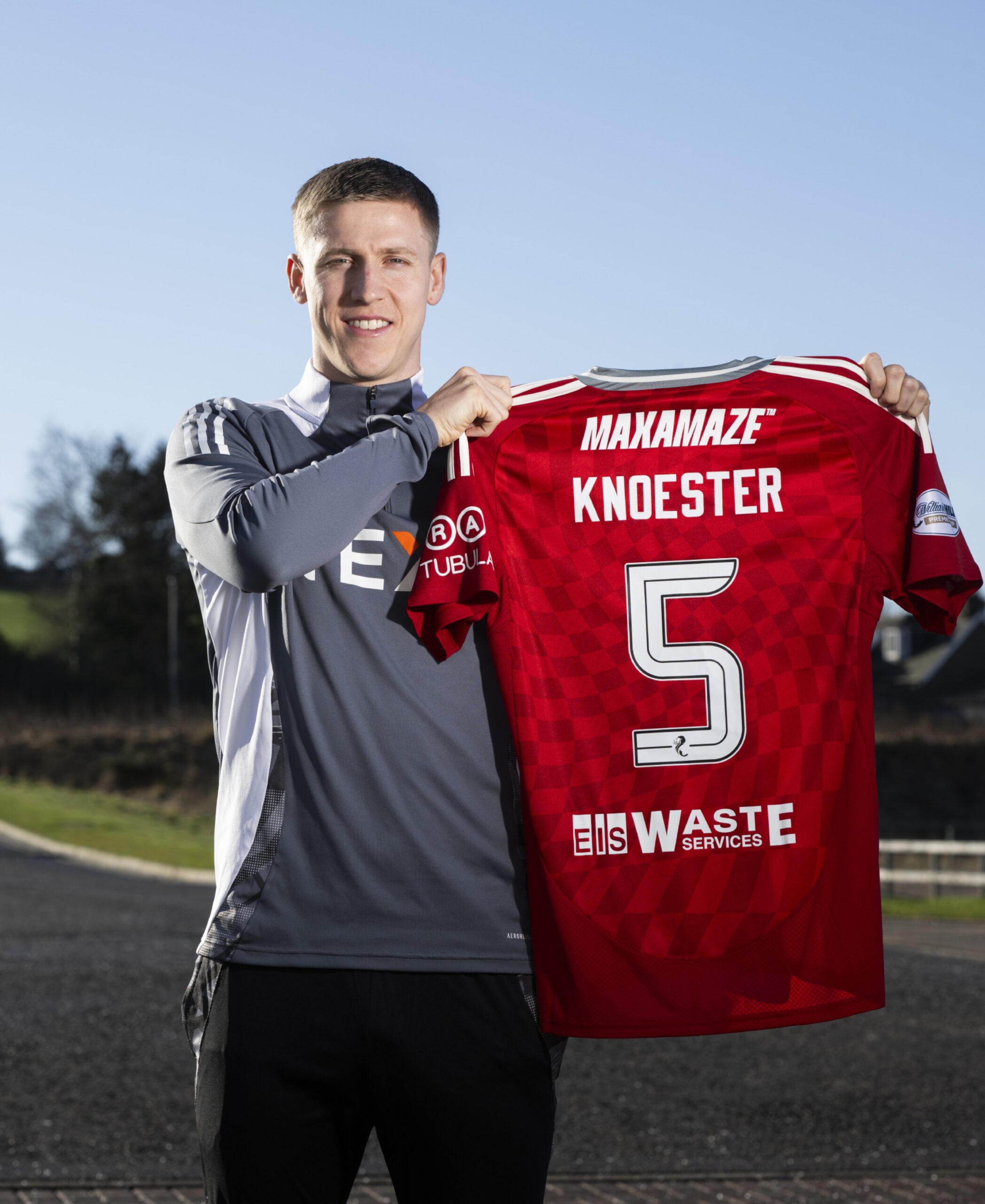 New Aberdeen signing Mats Knoester holds up his red club shirt with his name and number five on the back at the club's Cormack Park training facility. 