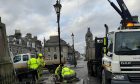 Workmen in high-vis vests work to remove heritage lights from The Square in Huntly, with the help of a crane.