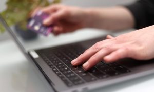 Person typing on laptop with bank card in other hand