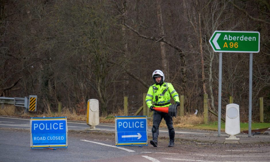 Police road closed dign as officer in yellow lays down a cone.