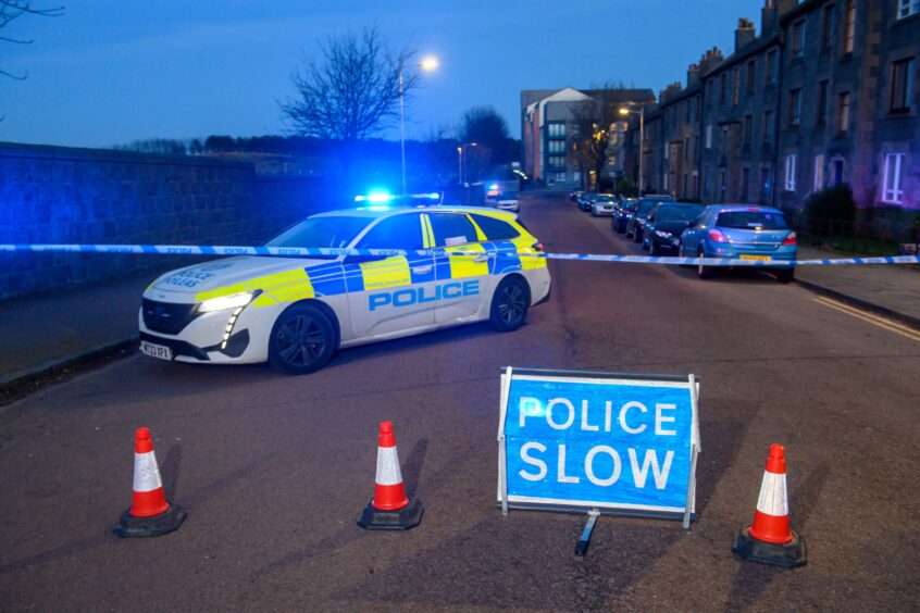 Police car and blue police tape block the road.