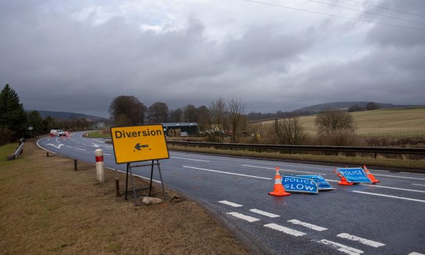 Cone and blue police road closed sign block the road alongside a yellow diversion sign.