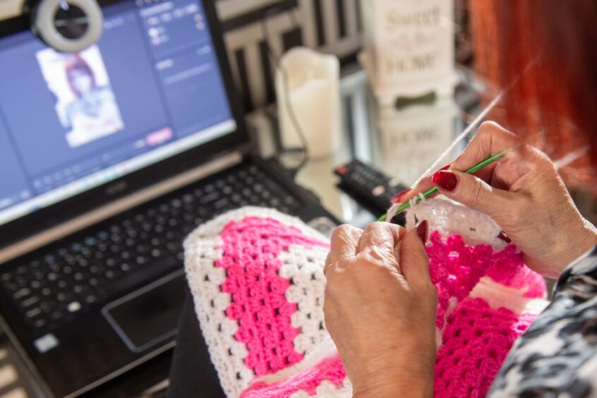 May knitting in front of the computer and camera for her live stream on TikTok.