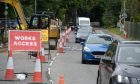 Red works access sign with cones on the left as traffic passes the single carriageway roadworks.