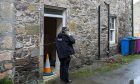 A police officer stands at the door of a property in Forres.