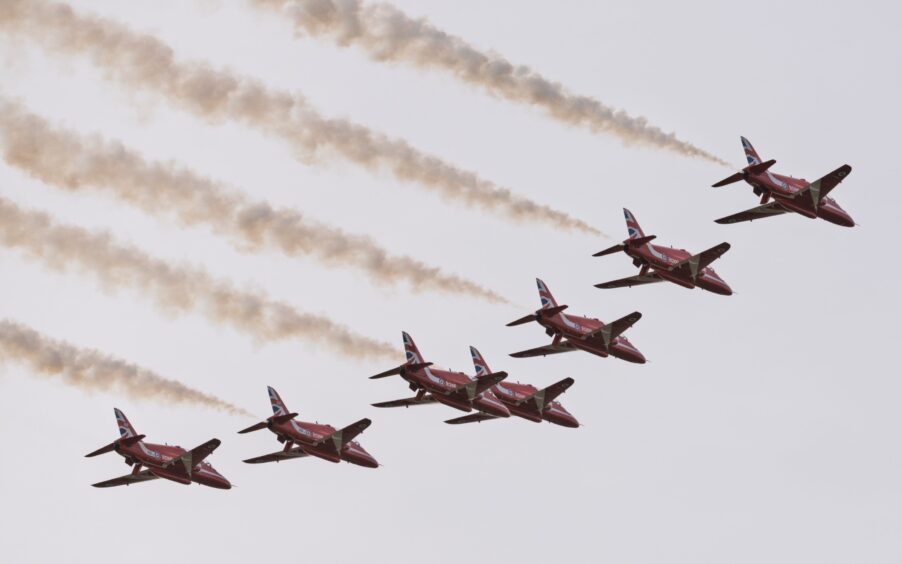 Seven Red Arrows aircrafts lined up with smoke flares.