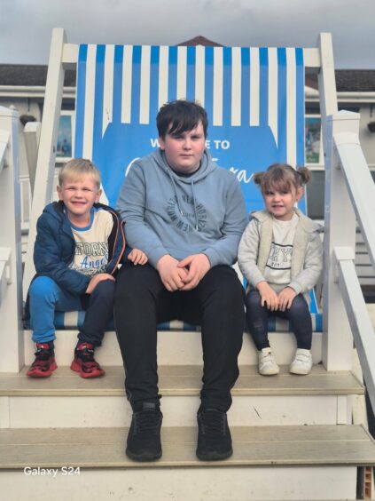 Kaden Askew from wick pictured with his Brother Danny and sister Abi-lee, sitting on a large beach deck chair.