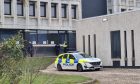 Police car pictures next to concrete wall of Dyce Academy as police stand guard at the main entrance.