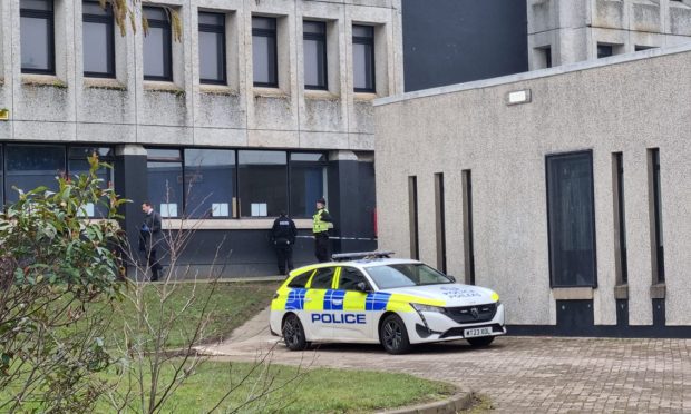 Police car pictures next to concrete wall of Dyce Academy as police stand guard at the main entrance.