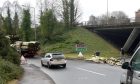 The lorry is to the left. Part of its load of logs can be seen to the right, blocking the road.