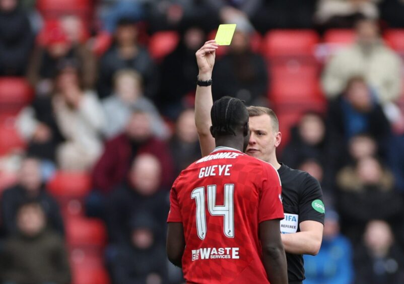 Referee Ross Hardie shows Aberdeen's Pape Gueye yellow card. Image: Shutterstock.