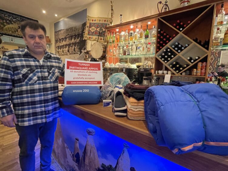 Owner Mustafa Calisir, standing beside the bar holding a red and white sign.