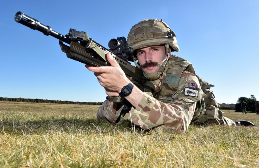 Corporal Jake Noble holding a rifle wearing his military uniform while lying flat on his stomach.