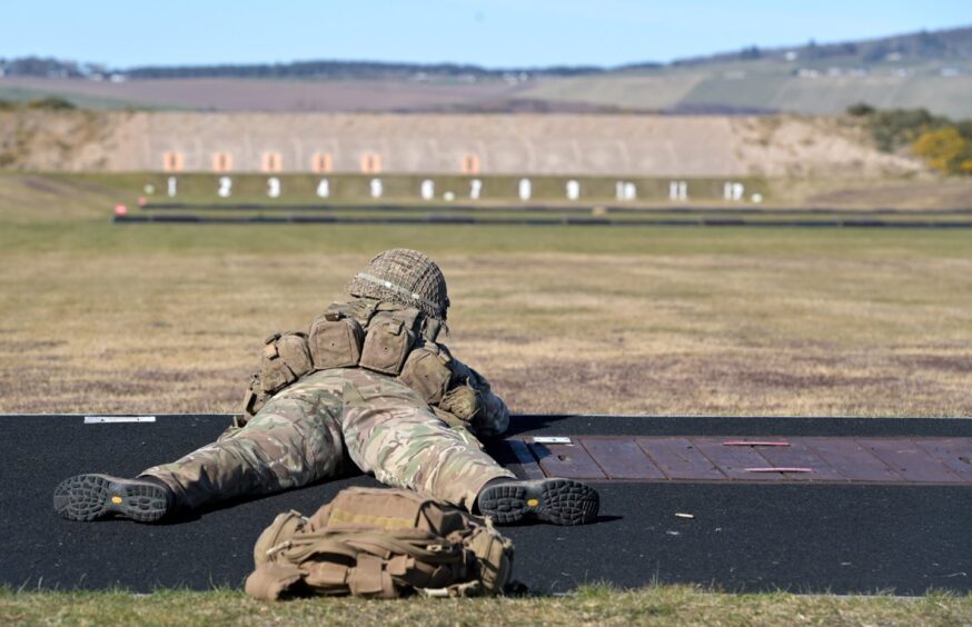 Soldier dressed in camouflage lies flat on their stomach while shooting at rifle range.