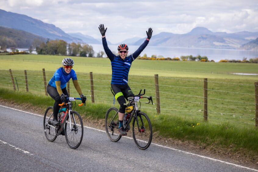 Two cyclist side by side on the road as a rider lifts his arms in the air. 