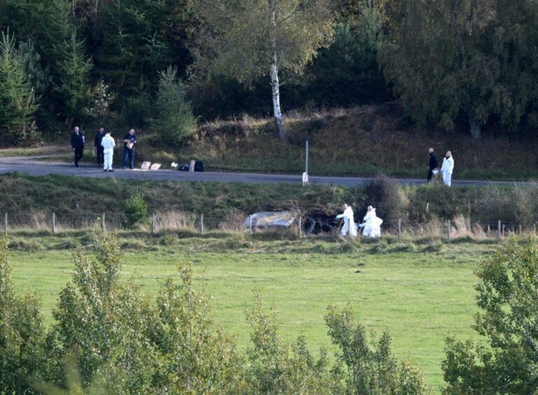 Forensic officers pictures at the scene of a crash, from a distance.