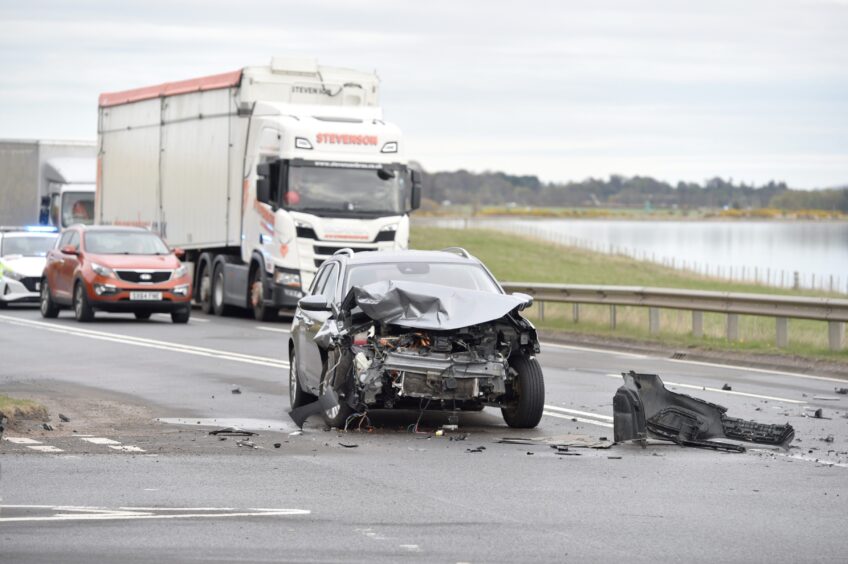 Silver car with severe damage to the front of the vehicle lies in the middle of the road as traffic builds to the rear.