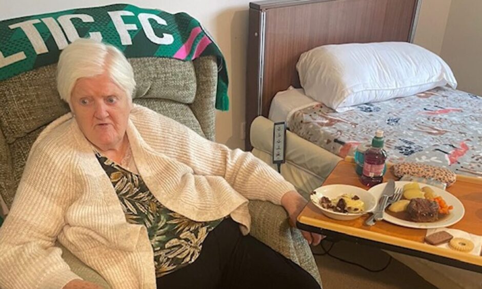 Siwar's grandmother witting in an arm chairr weating a cream cardigan with a green celtic scarf draped along the top with a table to her side.