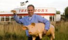 The Horn owner Kenny Farquharson holds a bacon roll and plastic pig outside the diner