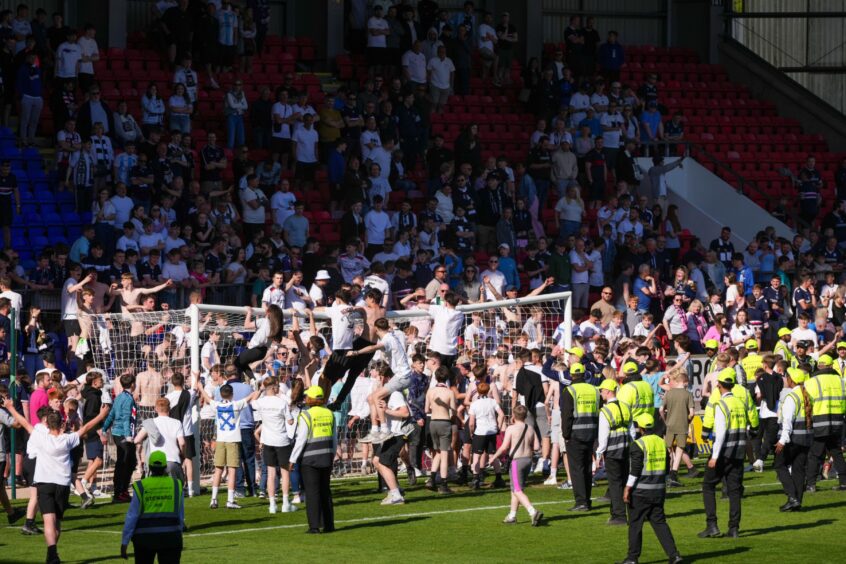 Dundee fans climb on the goal posts as they invade the McDiarmid Park pitch in celebration at full-time after their team avoided a relegation play-off. Image: Shutterstock.